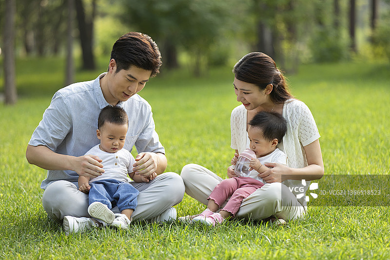 年轻父母在公园陪龙凤胎宝宝玩耍图片素材