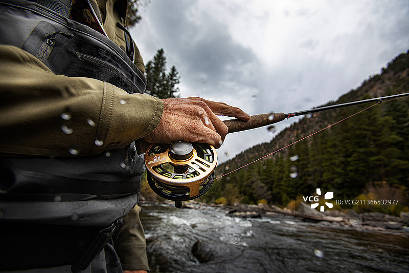 飞蝇钓鱼者手持鱼竿和卷线轮图片素材