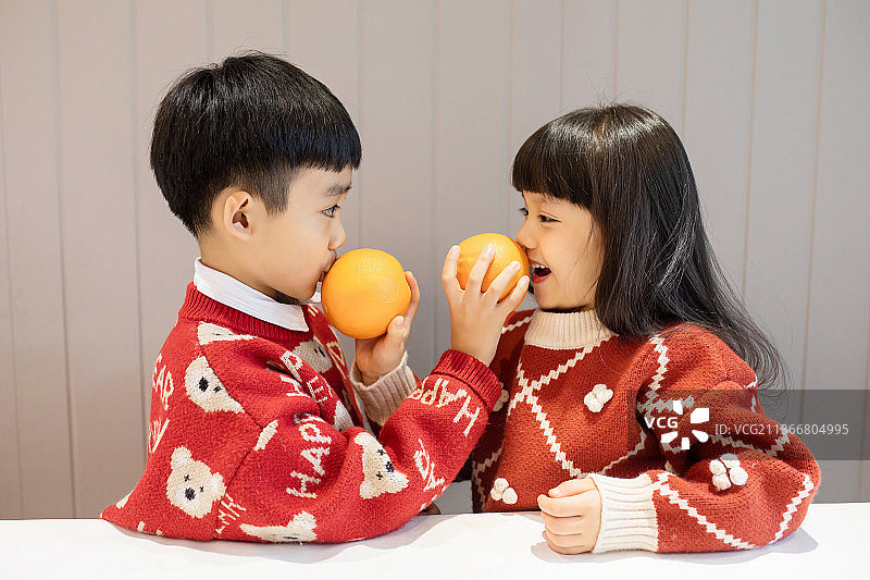 穿红色毛衣玩橙子的可爱兄妹俩图片素材