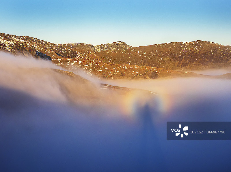 英国湖区，从红色山崖顶峰看到的破晓时分，赫尔威林山脉与伸出谷雾的步履边缘，以及摄影师的影子在雾中投射出的布罗肯幽灵图片素材