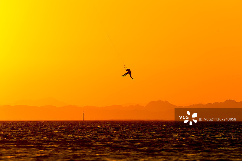 日落时，鸟儿在天空下飞过海面的剪影图片素材