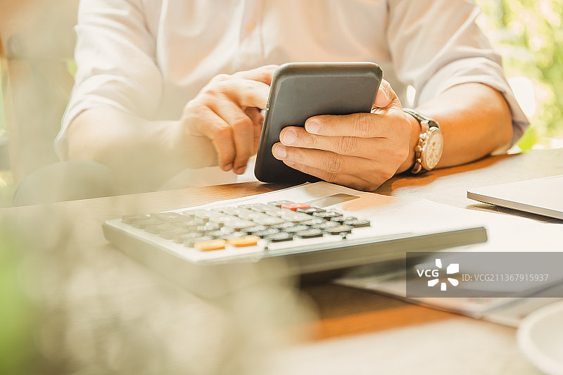 在木桌上使用智能手机和计算器的泰国商人图片素材