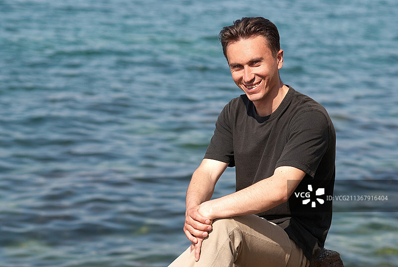 年轻男人的肖像，坐在海边的微笑的年轻男人的肖像图片素材