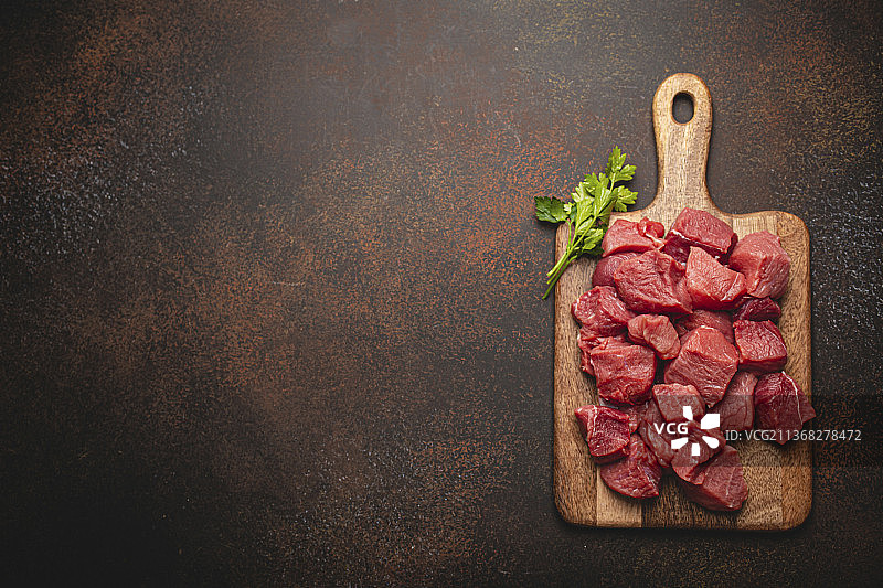 切成立方体的生牛肉和一束新鲜的欧芹在木制砧板上图片素材