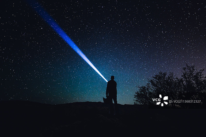 夜晚，站在美国亚利桑那州星空下的持手电筒男人剪影图片素材