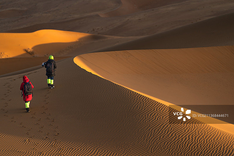 两位已经退休的女性摄影爱好者拿着单反相机和三脚架在巴丹吉林沙漠寻找拍摄机位（镜头背后的故事）图片素材