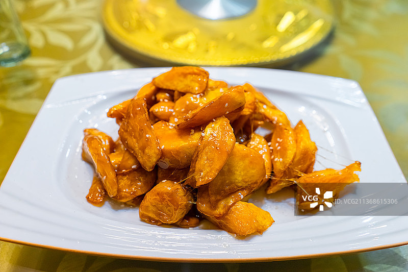 中国餐饮行业，一盘金黄色的拔丝地瓜，一只手拿着筷子夹起一块红薯拉丝图片素材