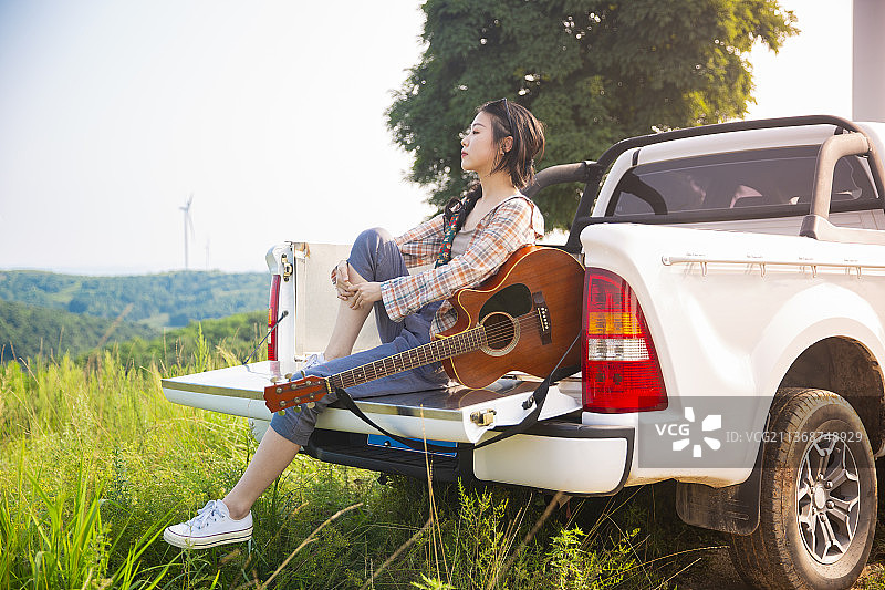 年轻女子户外郊游，带着吉他坐在皮卡车里图片素材