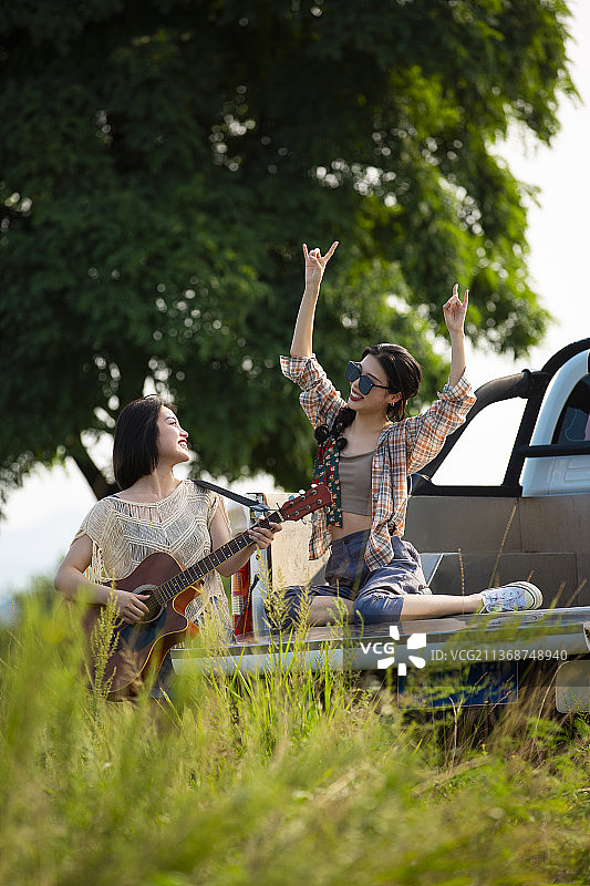 年轻闺蜜户外旅行坐在皮卡车里弹奏吉他唱歌跳舞玩耍图片素材