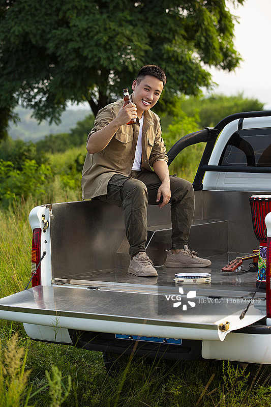 年轻男子户外旅行，坐在皮卡车里喝啤酒放松玩耍图片素材