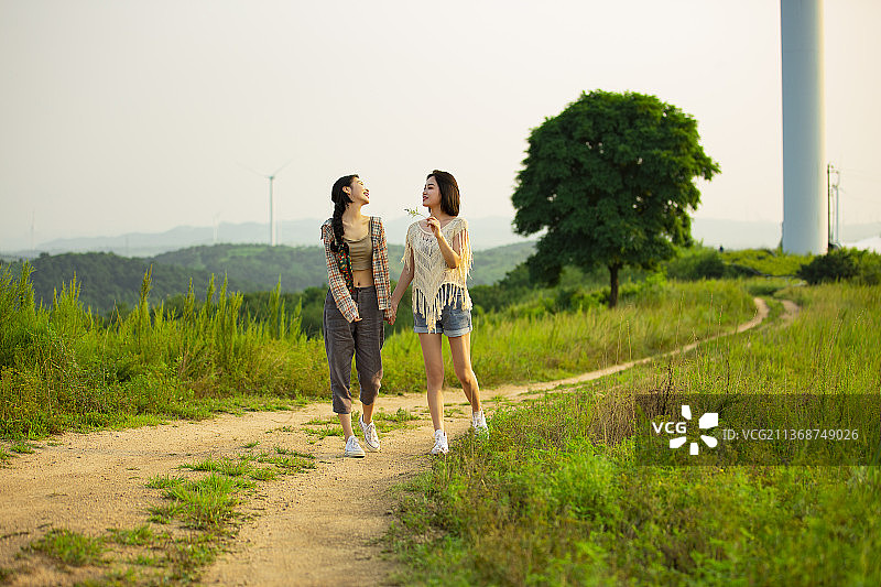 年轻闺蜜户外郊游，手牵手走在乡村的小路上嬉戏打闹图片素材
