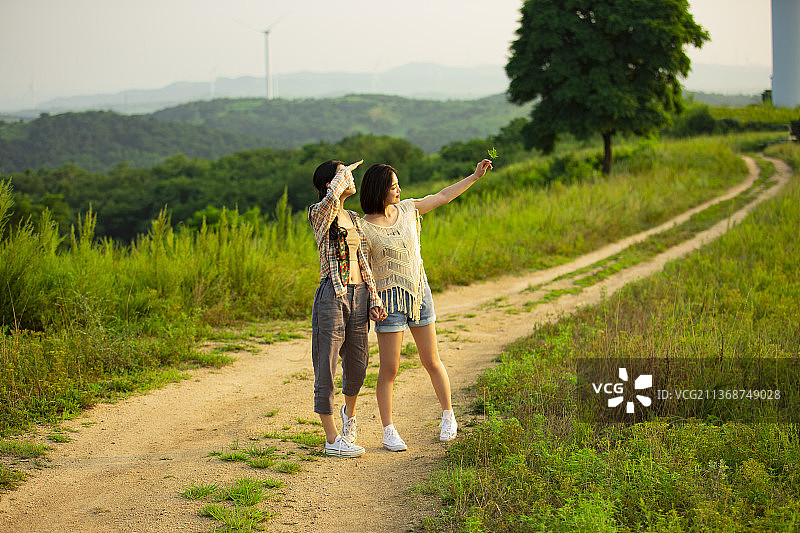 年轻闺蜜户外郊游，手牵手走在乡村的小路上图片素材