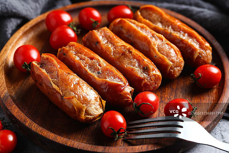 烤肠和圣女果放在木盘里图片素材