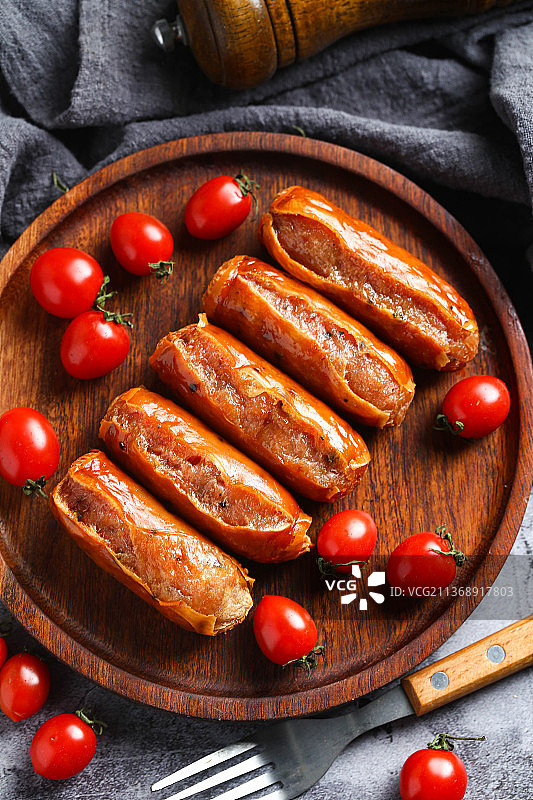 烤肠和圣女果放在木盘里图片素材