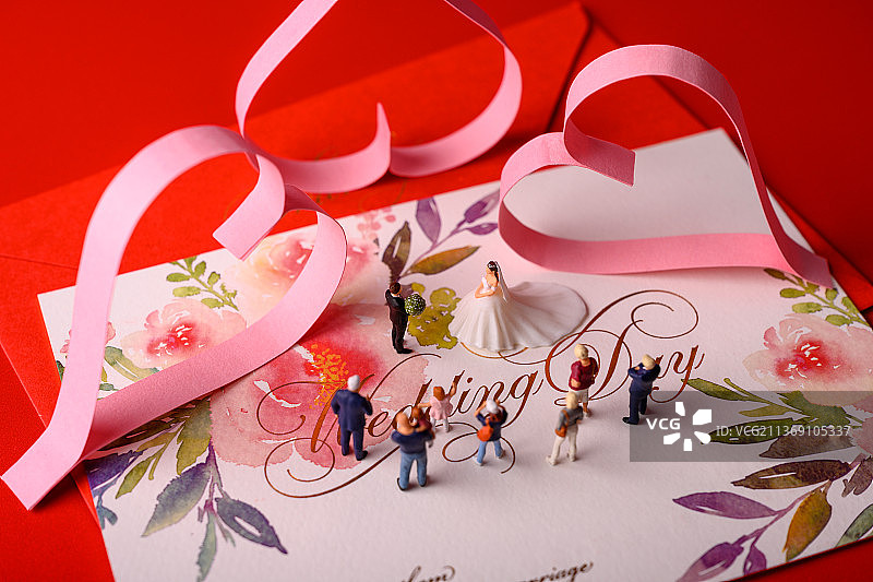 红色背景上放着的婚礼请柬和微缩景观婚礼图片素材