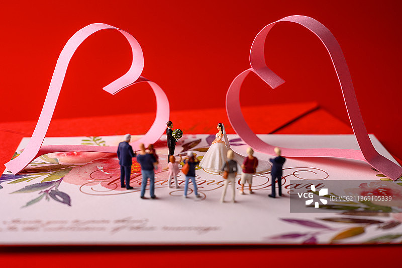 红色背景上放着的婚礼请柬和微缩景观婚礼图片素材