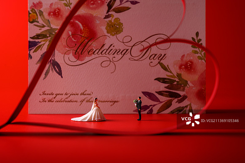 红色背景上放着的婚礼请柬和微缩景观婚礼图片素材