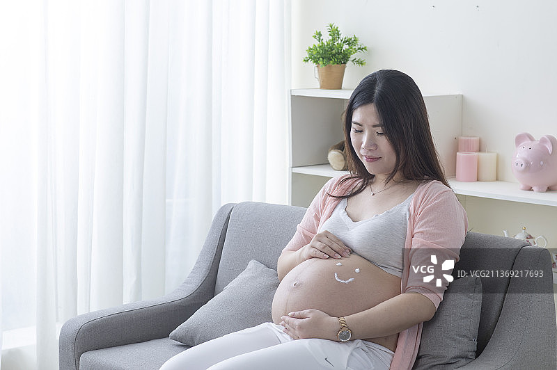 孕妇肚子上涂鸦着笑脸的图案手摸肚子坐在沙发上图片素材