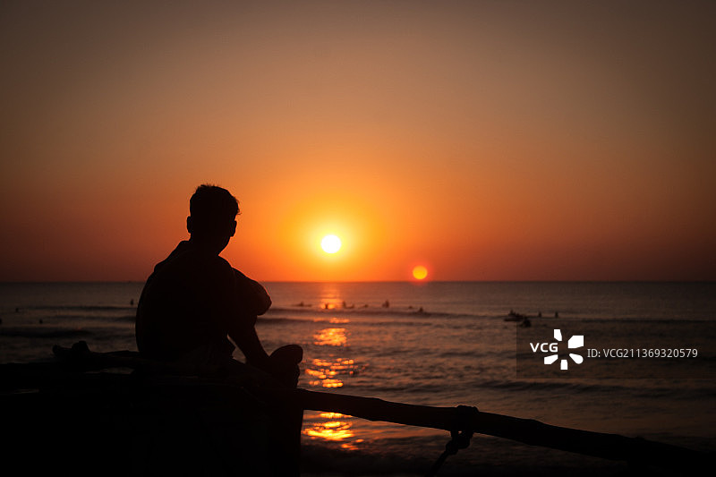 俯瞰大海的渔夫，日落时坐在海滩上对着天空的男人剪影图片素材