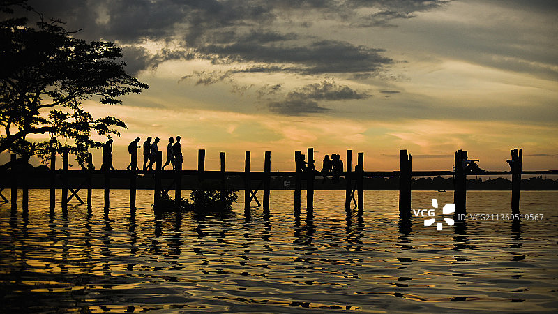 日落时乌本桥上的人们在天空的映衬下剪影图片素材