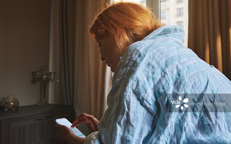 红发女人在家使用智能手机进行网上购物图片素材