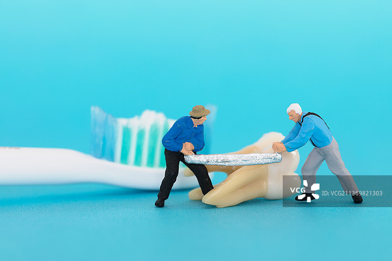 两名微缩工人用锯锯开一颗牙齿图片素材