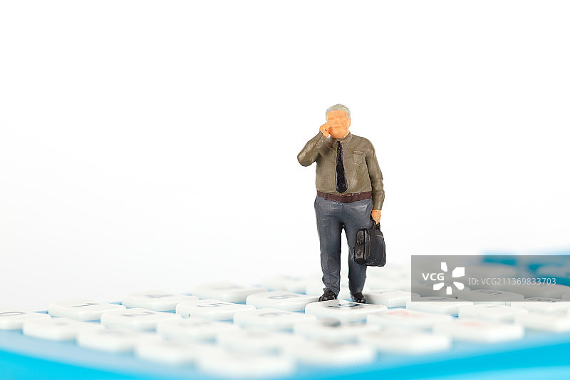 商人人偶站在计算器上打电话图片素材