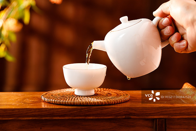 人拿着白色茶壶向茶杯倒茶图片素材