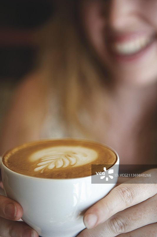 女人手捧一杯带有奶泡图案的卡布奇诺图片素材