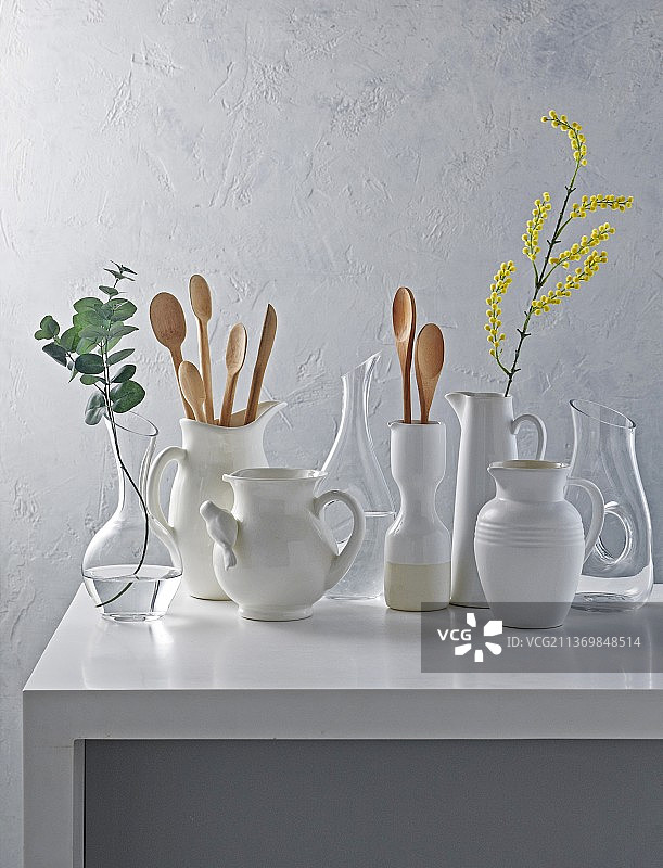 白色桌子上的白色醒酒器和陶瓷罐，一些有鲜花，一些有木勺图片素材