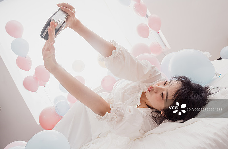 年轻女人躺在床上用宝丽来自拍图片素材
