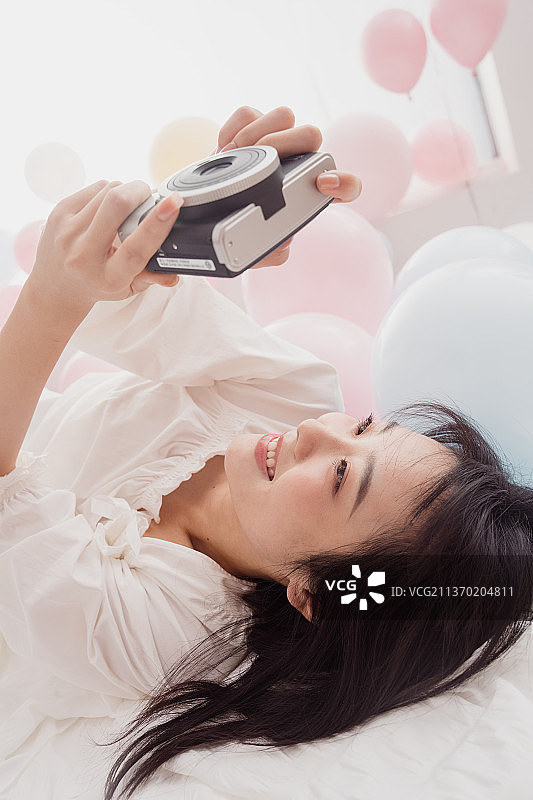 年轻女人躺在床上用宝丽来拍照图片素材