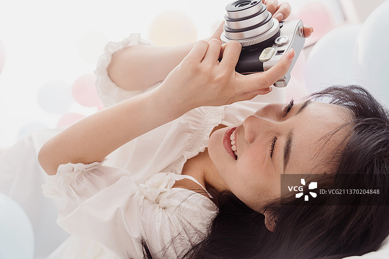 年轻女人躺在床上用宝丽来拍照图片素材