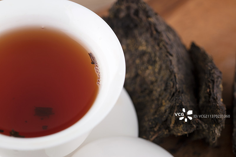 红润的茯茶茶汤在盖碗里及旁边的茶块图片素材