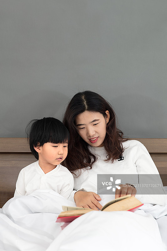 坐在床头的年轻妈妈给孩子讲故事图片素材