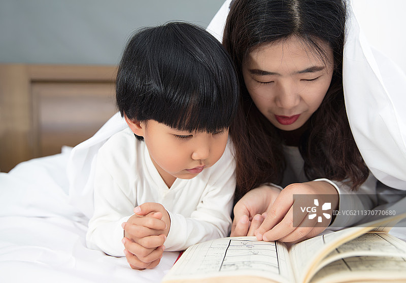 年轻妈妈和女儿在床上讲故事书图片素材