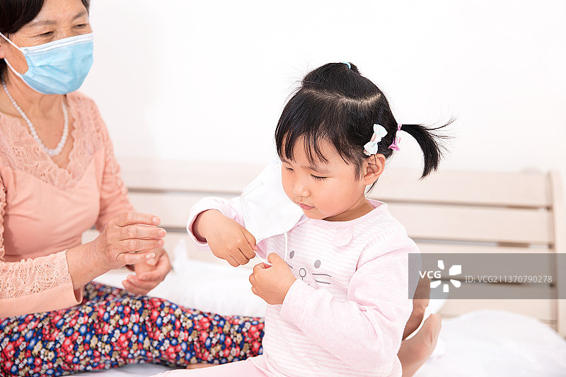 中国小姑娘学着奶奶戴上口罩图片素材