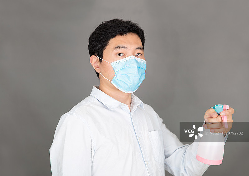 戴着口罩手拿消毒液喷洒的男士图片素材