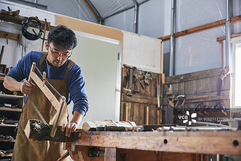 中年男人在工作坊进行手工锯木图片素材