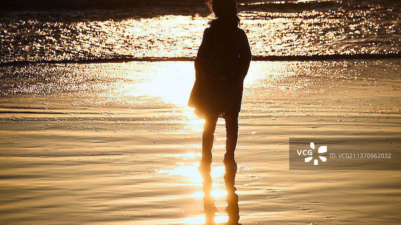 日落时分，女子站在海滩上的剪影图片素材