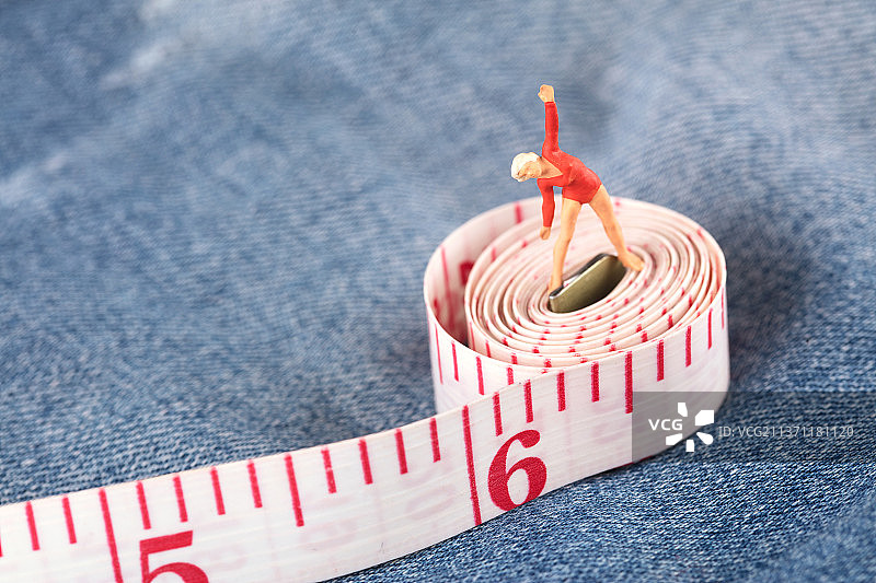 年轻的美女微缩人偶在软尺上做健身操图片素材