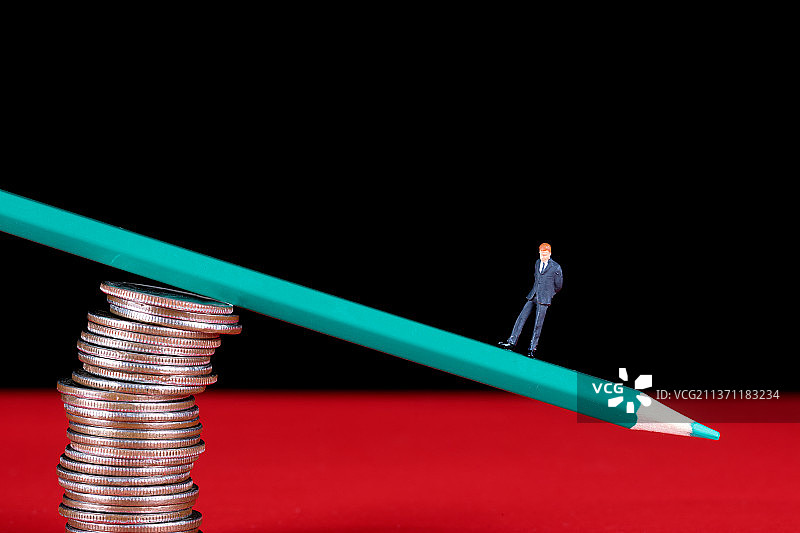 一摞硬币上失衡的彩铅笔和一头微缩商人模型图片素材