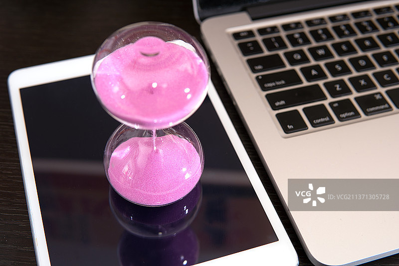 沙漏在电脑旁的ipad上面图片素材