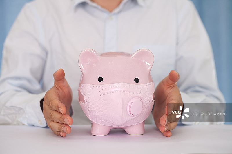 男士双手呵护着一个戴口罩的小猪储蓄罐图片素材