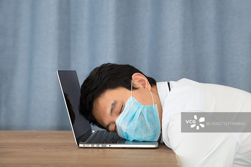 戴口罩的男士趴在电脑键盘上睡着了图片素材