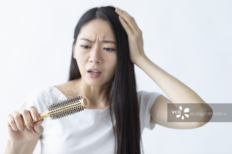 东方美女一手拿着卷发器一手抚摸自己的头发皱眉头图片素材