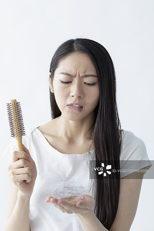 东方美女拿着卷发器看着自己的掉落的头发皱眉头图片素材