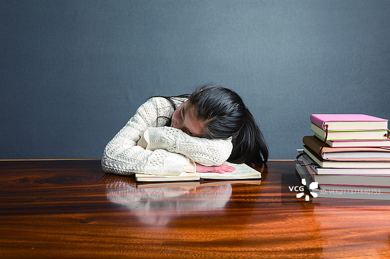 灰背景，大桌子，写作业写的有些累了，打哈欠的穿白色毛衣的女孩图片素材