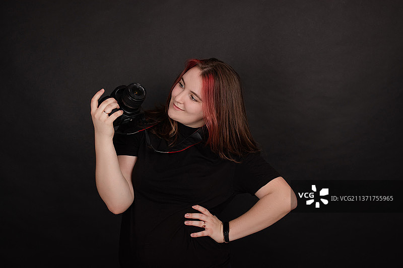 手持专业相机、在黑色背景前摆姿势的红发女孩图片素材