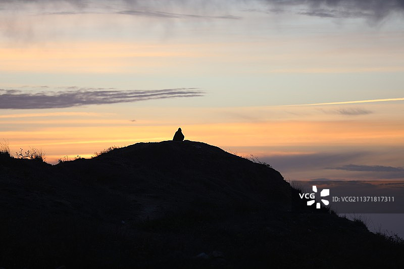 戴帽子坐在山上观看日落的男人轮廓图片素材
